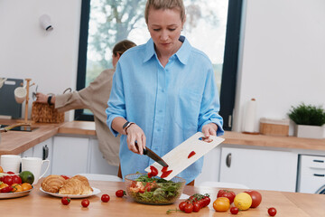 Middle age woman preparing a healthy salad in bright kitchen, promoting active lifestyle, wellness, and wellbeing with fresh vegetables and natural light.