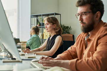 Young adult Caucasian woman and young adult Caucasian man working at computer monitors in modern office, multiethnic team developing neural network technology in collaborative workspace