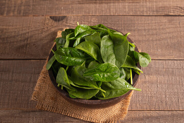 Green baby spinach leaves in wooden bowl on wooden background. Organic food concept. 