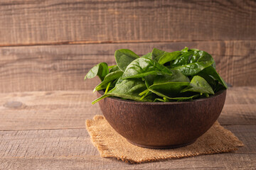 Green baby spinach leaves in wooden bowl on wooden background. Organic food concept. 