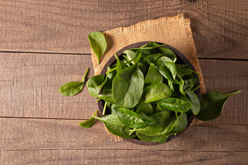 Green baby spinach leaves in wooden bowl on wooden background. Organic food concept. 
