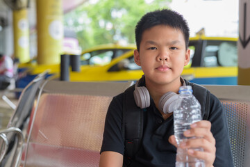 Thai teen boy wearing headphones and drinking water from bottle taxis in background