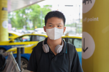 Thai boy with facial mask with taxis in background wearing headphones