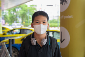 Thai boy with facial mask with taxis in background wearing headphones