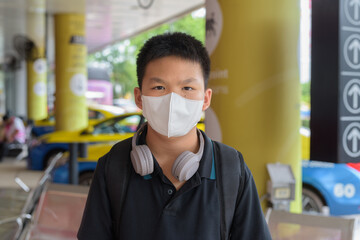 Thai boy with facial mask with taxis in background wearing headphones