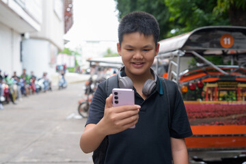 Thai boy with headphones standing by tuk tuk taxis