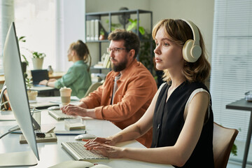 Caucasian young adult woman wearing headphones working on computer with Caucasian middle aged man...