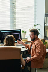 Caucasian middle aged man explaining neural network code to Caucasian young adult woman sitting at...