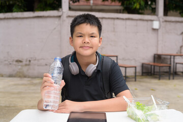 Thai boy eating salad and using wireless technology at outdoor table