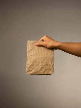 Hand Holding a Wrinkled Kraft Paper Bag in Studio Lighting