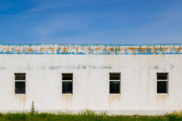 Weathered building with decayed Kyrgyzstani ornament and four windows in grassy area