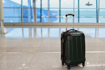 A suitcase stands alone on the floor in an airport terminal, symbolizing travel and waiting.