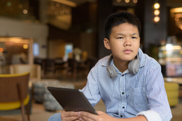 Thai boy using digital tablet computer at cafe with headphones