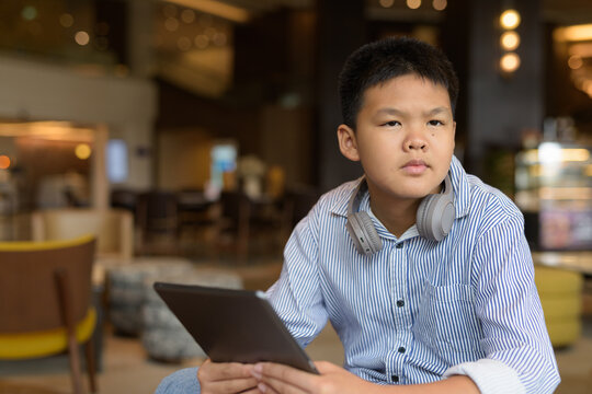 Thai boy using digital tablet computer at cafe with headphones