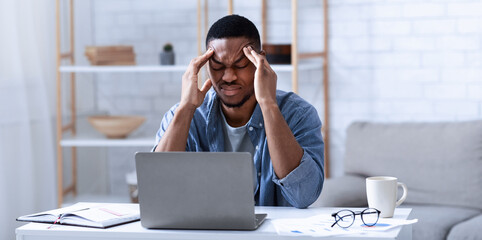 African American Businessman Having Headache Sitting At Laptop Computer Working From Home. Black Man Massaging Temples Suffering From Migraine Pain Indoor. Selective Focus