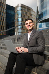 Business professional enjoys a sunny afternoon working on laptop outdoors amidst modern skyscrapers in an urban setting