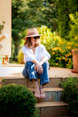Full length of a blond haired mature woman sitting at stone step in back yard at home