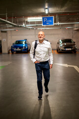 Senior business man walking in the park garage and holding a computer laptop in his hand