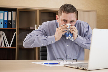 Man sneezes while working at his desk in a modern office environment during the day