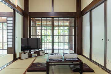 Traditional Japanese room with tatami mat floor and low table with cushions, sliding doors open to...