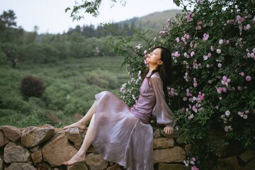 Young woman in a flowing purple dress by blooming flowers.