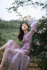Elegant young woman in a flowy dress amidst blooming flowers.