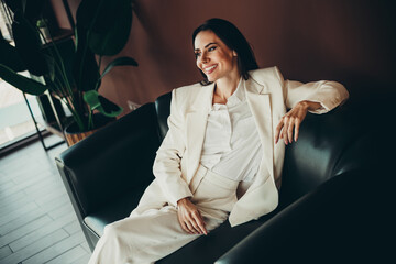 Confident businesswoman in stylish formalwear lounging on an elegant sofa in a modern office...
