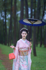 Traditional Japanese Woman in Furisode Kimono with blue wagasa umbrella in Pine Forest. Cultural...
