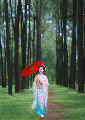 Traditional Japanese Woman in Furisode Kimono with red wagasa umbrella in Pine Forest. Cultural fashion and nature harmony.