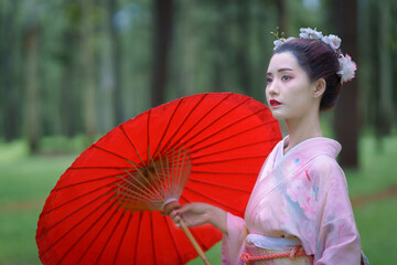 Traditional Japanese Woman in Furisode Kimono with red wagasa umbrella in Pine Forest. Cultural fashion and nature harmony.