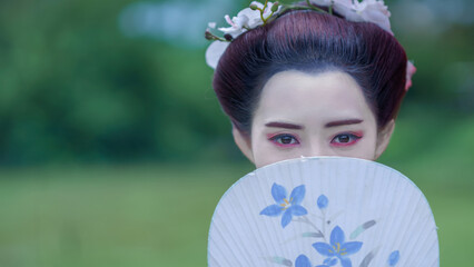 Traditional Japanese  pretty woman in Furisode Kimono holding fan and posting in green natural Pine...