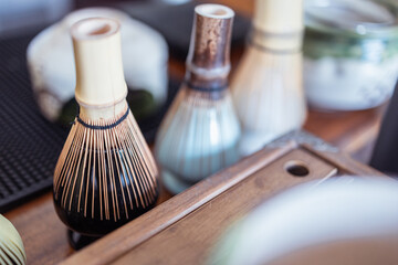 Bamboo tea whisk with ceramic cups on wooden tray close up