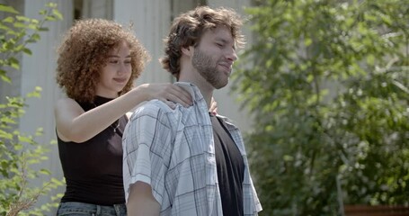 A young woman gives a relaxing shoulder massage to her boyfriend or husband outdoors on a sunny day. They look happy and in love. - Powered by Adobe