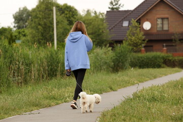 A young girl in a blue jacket and black pants walks home with her dog along an alley among the...