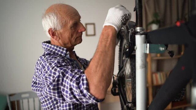 Elderly man fixing bicycle at home, tightening fender on wheel using wrench. Concept of maintenance, fixing, repair and preparing bicycle for new season