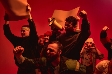 A group of diverse individuals passionately protest with signs and a megaphone under dramatic red...