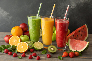 Three glasses of fresh fruit juice with watermelon, orange, apple, kiwi, and berries on wooden table