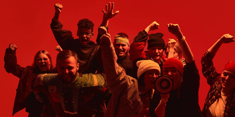 A diverse assembly of demonstrators raises their fists against a backdrop illuminated in intense...