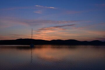Serene Sunset Reflections Over Calm Waters with a Sailboat in the Background