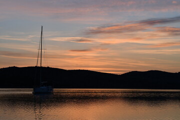 Serene Sunset Over Tranquil Waters with Sailboat Silhouette