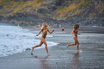 Female friends running on volcanic beach