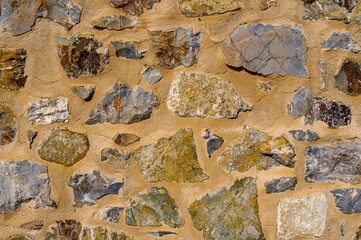 Beautiful background of yellow clay wall with natural stones embedded in it, different in texture, size and structure. Horizontal photo