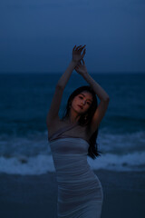 Young woman in a dress dancing by the beach at dusk.