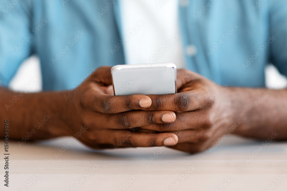 Poster Closeup Shot Of African American Man Sitting At Desk And Using Smartphone, Cropped Image Of Unrecognizable Black Guy With Mobile Phone In Hands Texting With Somebody Or Browsing New App