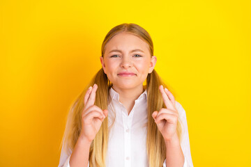 Hopeful young student crossing fingers for good luck on bright yellow classroom background