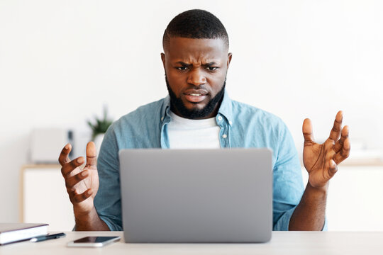 Deadline Stress. Annoyed black man sitting at workplace looking at laptop screen, african american freelancer guy suffering business problems while working online on computer at home office - Powered by Adobe