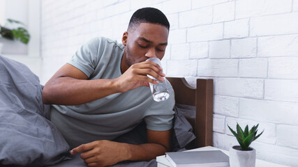 Black Man Taking Glass Of Water Lying In Bed, Hydrating Drinking In Bedroom At Home In The Morning,...