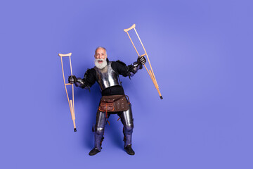 Mature man in knight armor holding crutches in a whimsical pose against a violet background