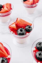 Colorful dessert cups with strawberries and blueberries on a white surface