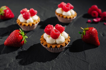 Delicious raspberry topped mini tarts with strawberries on a dark surface